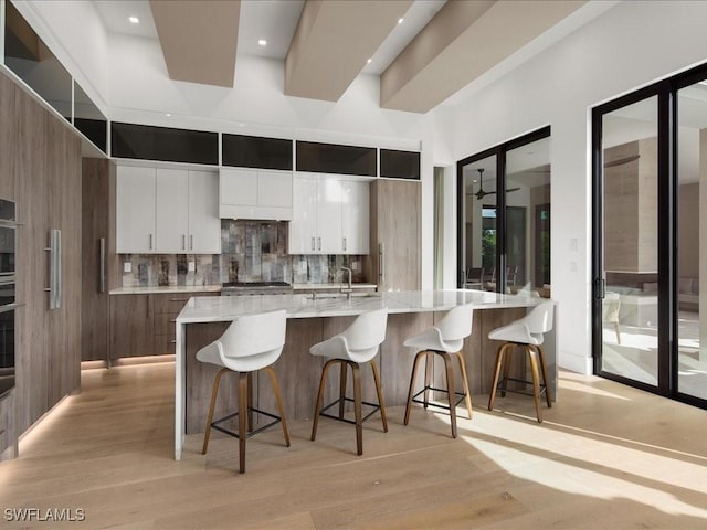 kitchen featuring white cabinetry, tasteful backsplash, a breakfast bar, and a large island with sink