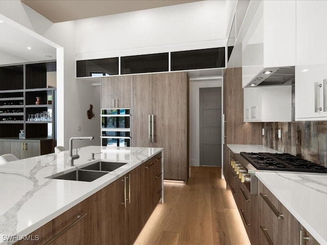 kitchen featuring white cabinetry, sink, light hardwood / wood-style floors, light stone countertops, and wall chimney exhaust hood