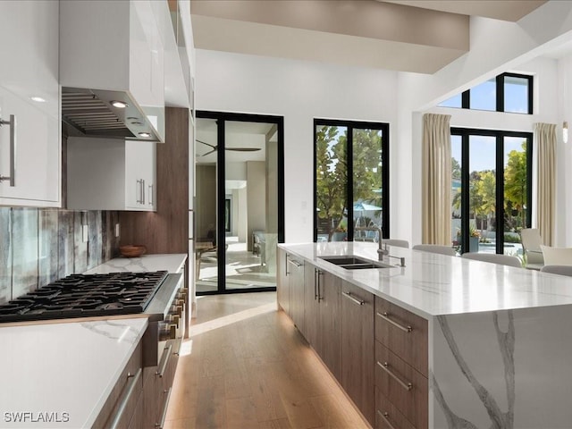 kitchen featuring wall chimney range hood, light hardwood / wood-style flooring, backsplash, white cabinets, and a kitchen island