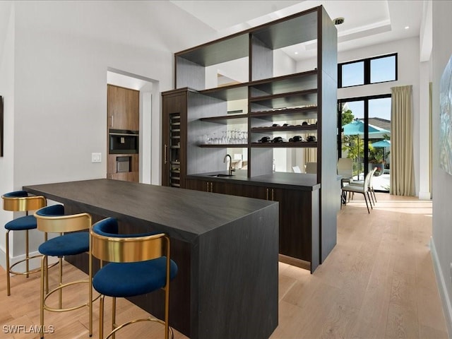 bar with a high ceiling, dark brown cabinets, sink, and light wood-type flooring