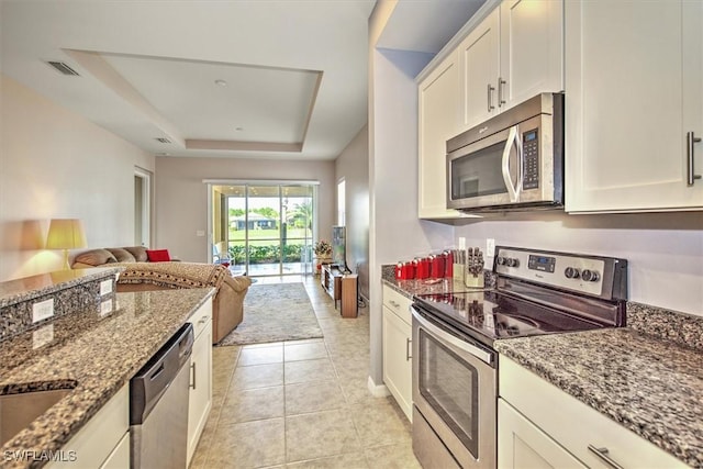 kitchen featuring a tray ceiling, dark stone counters, white cabinets, and appliances with stainless steel finishes