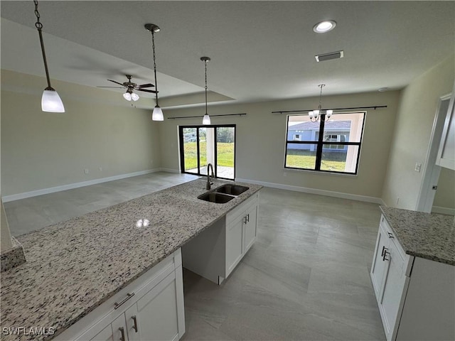 kitchen with light stone countertops, sink, white cabinets, and decorative light fixtures