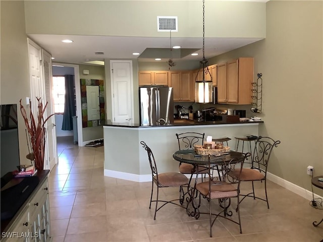 kitchen featuring light tile patterned flooring, decorative light fixtures, light brown cabinets, stainless steel fridge, and kitchen peninsula