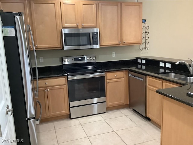 kitchen with dark stone countertops, light brown cabinets, light tile patterned flooring, a sink, and stainless steel appliances