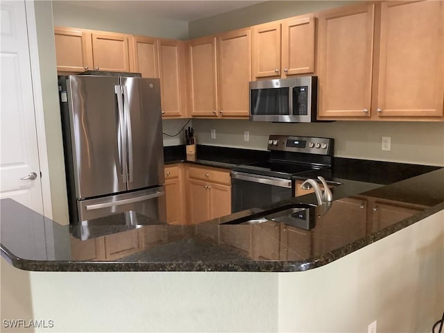 kitchen with a sink, appliances with stainless steel finishes, dark stone countertops, and light brown cabinets