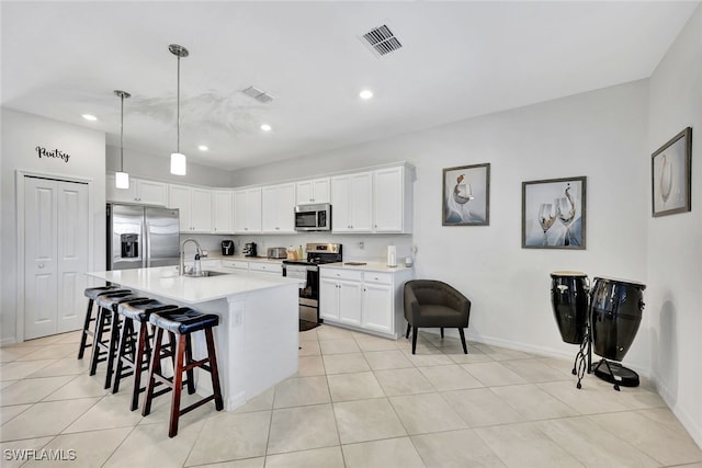 kitchen featuring sink, hanging light fixtures, appliances with stainless steel finishes, a kitchen island with sink, and white cabinets