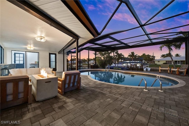 pool at dusk featuring a patio, a lanai, and an outdoor living space with a fire pit