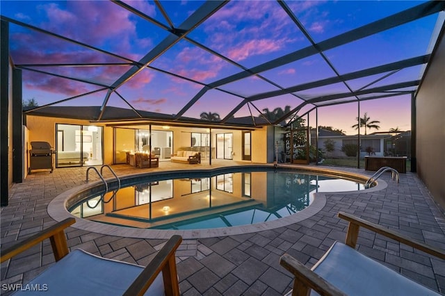 pool at dusk with an outdoor hangout area, a patio area, and glass enclosure