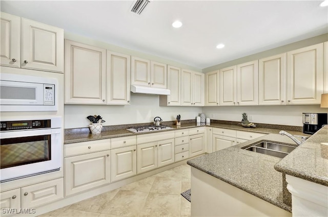 kitchen with light tile patterned flooring, sink, white appliances, dark stone counters, and cream cabinetry