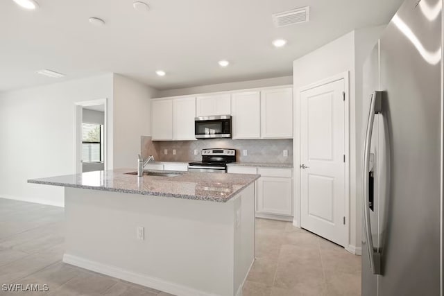 kitchen with sink, white cabinetry, stainless steel appliances, light stone counters, and an island with sink