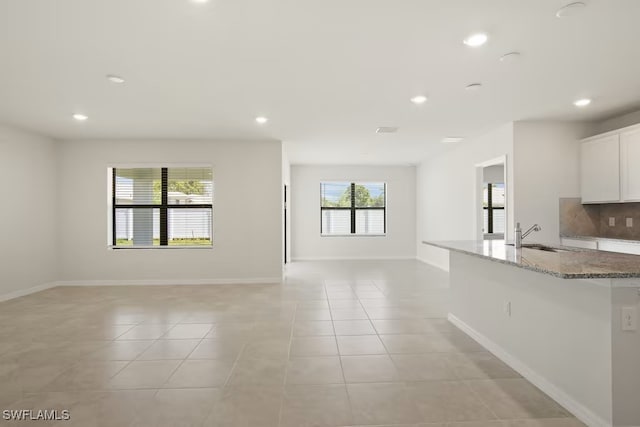 kitchen with sink, white cabinets, decorative backsplash, light tile patterned floors, and light stone countertops