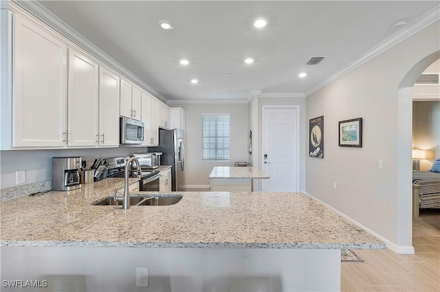 kitchen with appliances with stainless steel finishes, sink, white cabinets, ornamental molding, and light stone counters