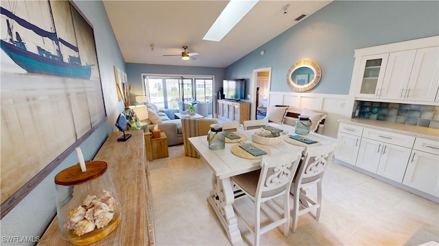 tiled dining space with ceiling fan and vaulted ceiling with skylight