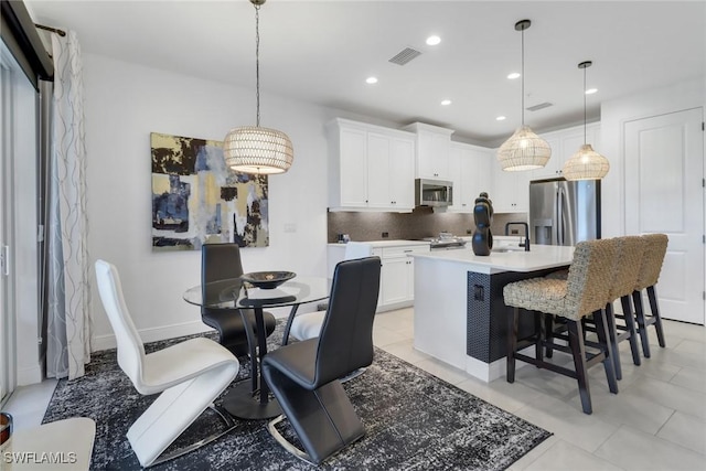 kitchen featuring appliances with stainless steel finishes, a kitchen island with sink, decorative backsplash, white cabinets, and decorative light fixtures