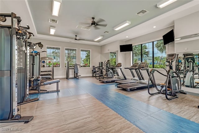 workout area with ceiling fan and a tray ceiling