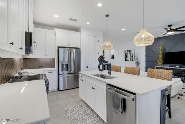 kitchen with a breakfast bar area, appliances with stainless steel finishes, a kitchen island with sink, white cabinets, and decorative light fixtures