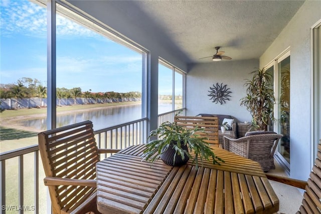 sunroom with ceiling fan and a water view