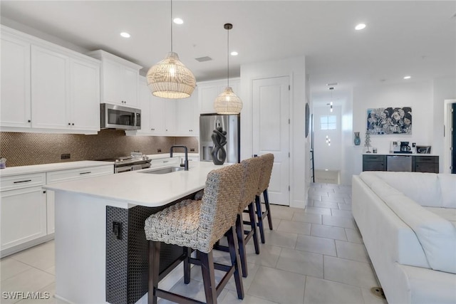 kitchen with appliances with stainless steel finishes, pendant lighting, sink, white cabinets, and a center island with sink