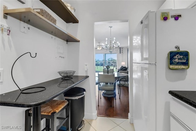 kitchen featuring a chandelier, dark stone countertops, freestanding refrigerator, light tile patterned flooring, and white cabinetry