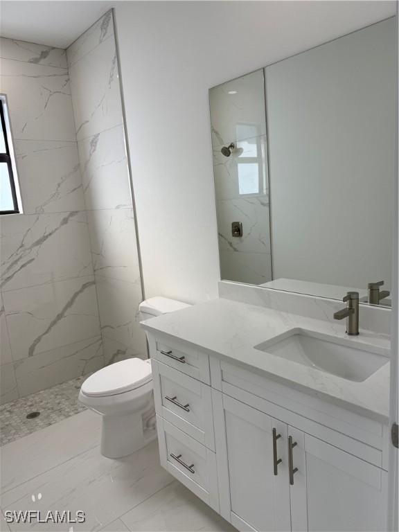 bathroom featuring vanity, a tile shower, and toilet