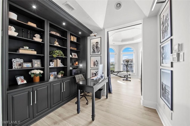 office area with built in shelves, a tray ceiling, and light hardwood / wood-style floors