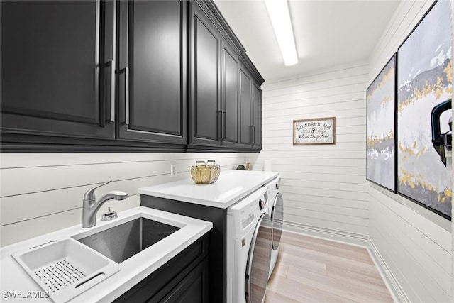 laundry area featuring cabinets, sink, washer and clothes dryer, and light hardwood / wood-style floors