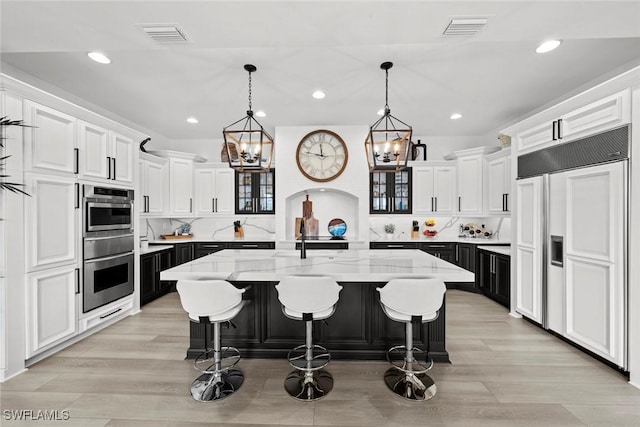 kitchen featuring white cabinetry, an island with sink, light stone countertops, and paneled built in refrigerator