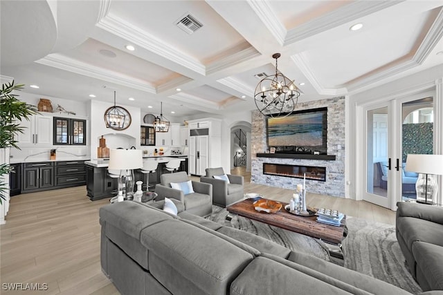 living room with beam ceiling, coffered ceiling, a fireplace, ornamental molding, and light wood-type flooring