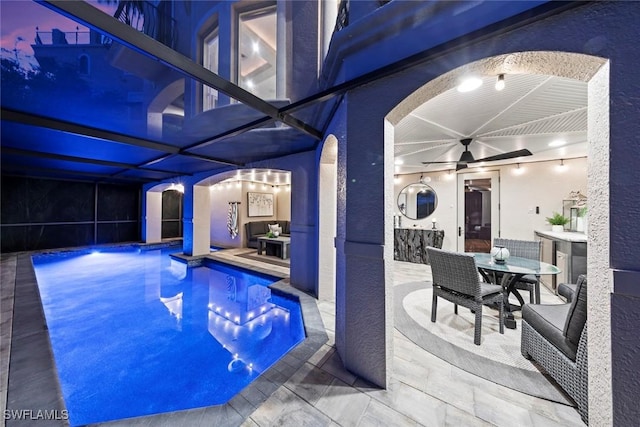 pool at dusk featuring ceiling fan, a lanai, and a patio