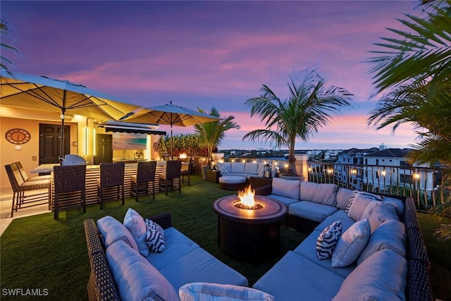 patio terrace at dusk featuring exterior bar, a yard, and an outdoor living space with a fire pit