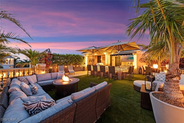 patio terrace at dusk featuring a lawn and an outdoor living space with a fire pit