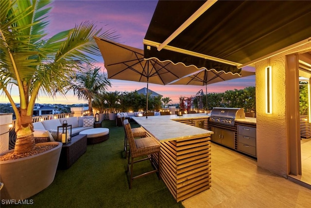 patio terrace at dusk with exterior bar, area for grilling, and an outdoor hangout area