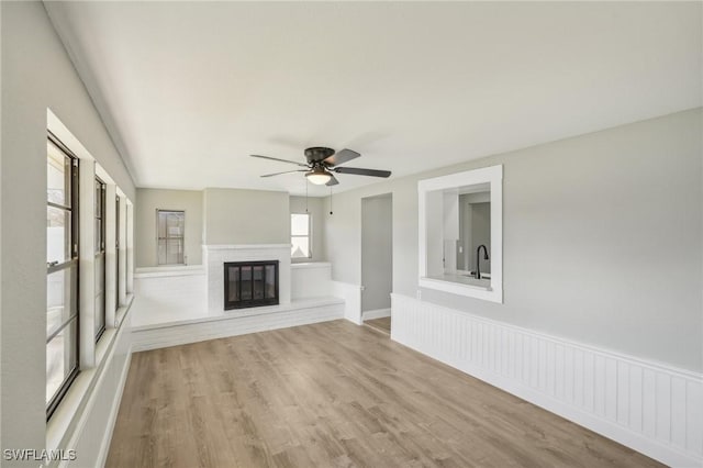 unfurnished living room featuring ceiling fan, a fireplace, sink, and light wood-type flooring