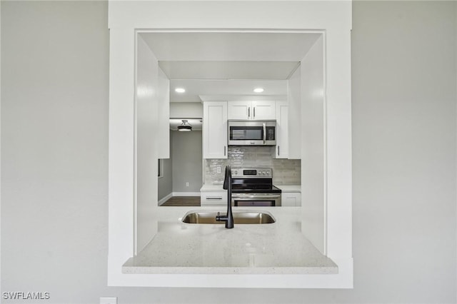 kitchen featuring sink, white cabinetry, appliances with stainless steel finishes, light stone countertops, and backsplash