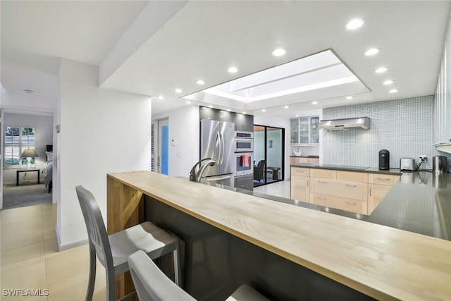 kitchen featuring wall chimney exhaust hood, modern cabinets, appliances with stainless steel finishes, a breakfast bar area, and backsplash