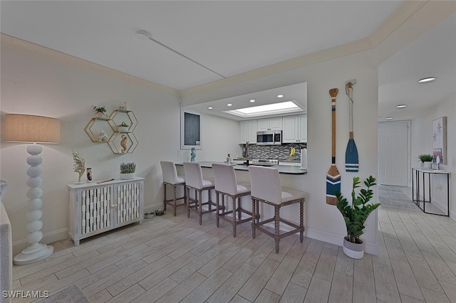 kitchen with tasteful backsplash, white cabinetry, a kitchen bar, kitchen peninsula, and light wood-type flooring