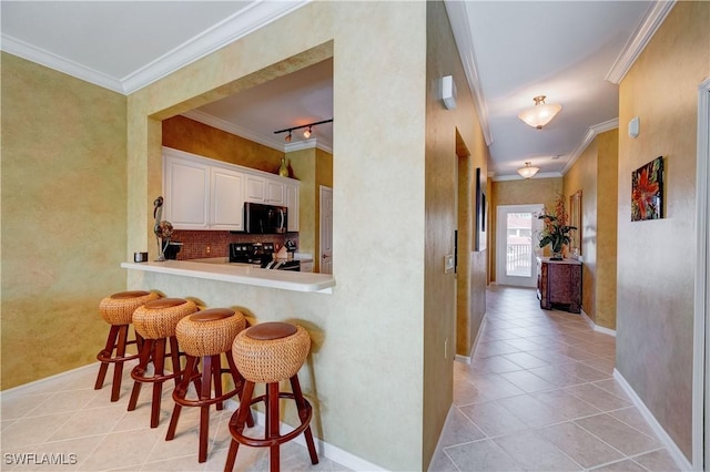 kitchen featuring light tile patterned floors, crown molding, white cabinetry, black electric range, and a kitchen bar