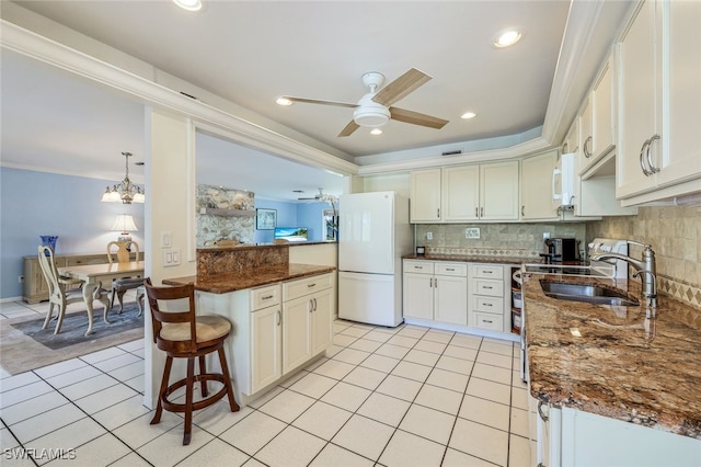 kitchen featuring a breakfast bar, dark stone countertops, white cabinets, white appliances, and backsplash