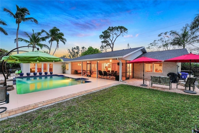 pool at dusk with outdoor lounge area, a patio area, and a lawn