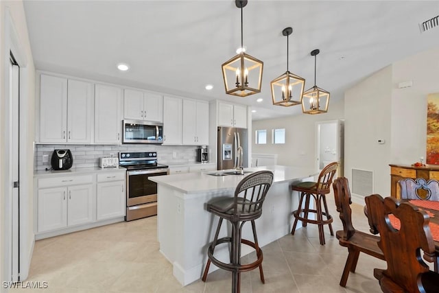 kitchen with a breakfast bar, hanging light fixtures, stainless steel appliances, an island with sink, and white cabinets