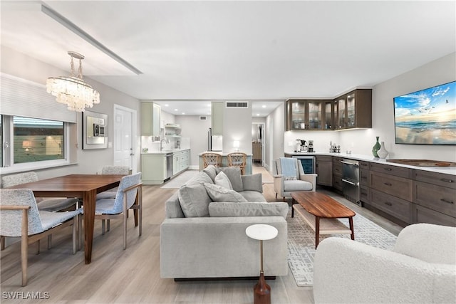 living room with wet bar, wine cooler, a chandelier, and light hardwood / wood-style flooring