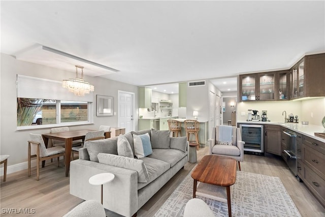 living room with wet bar, beverage cooler, a chandelier, and light wood-type flooring