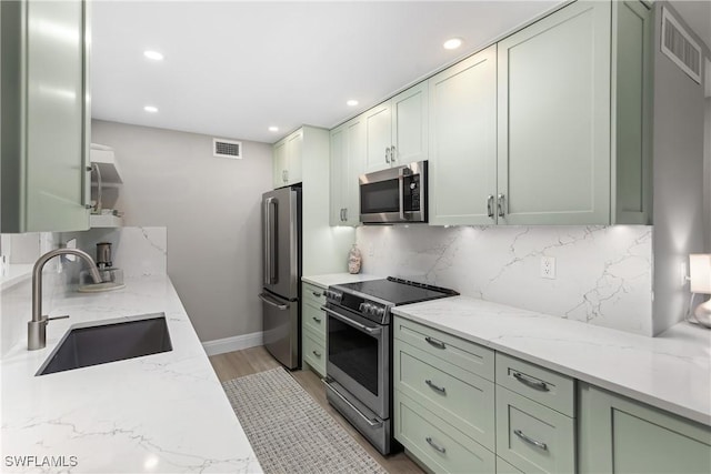 kitchen with sink, tasteful backsplash, stainless steel appliances, light stone countertops, and light hardwood / wood-style floors