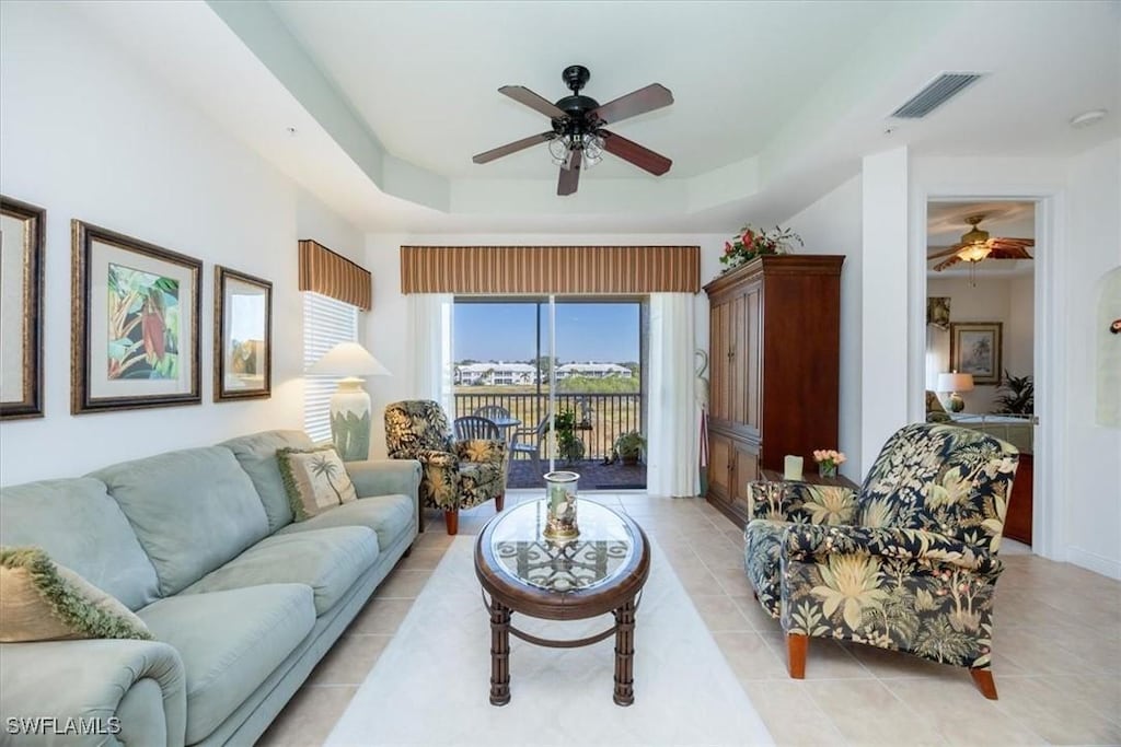 living room featuring a raised ceiling, light tile patterned floors, and ceiling fan