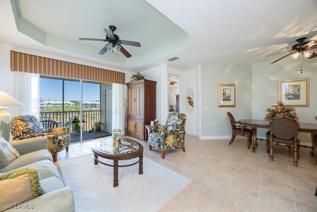 living room with light tile patterned floors, a tray ceiling, and ceiling fan