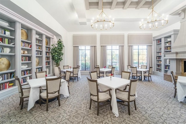 dining space with built in shelves, a notable chandelier, beamed ceiling, light colored carpet, and a premium fireplace