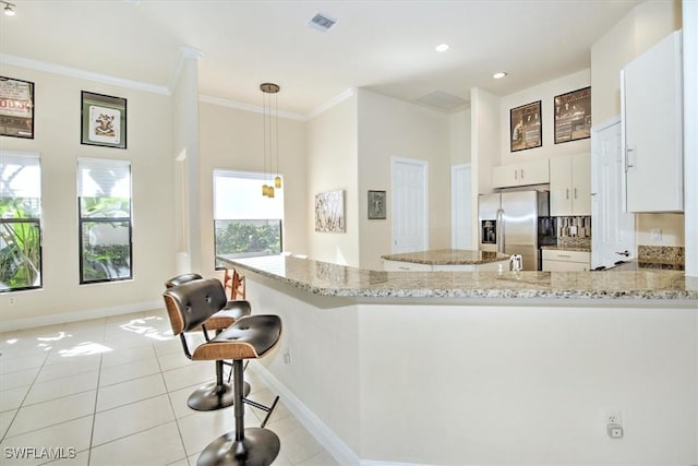 kitchen with pendant lighting, stainless steel fridge, white cabinetry, light stone counters, and kitchen peninsula