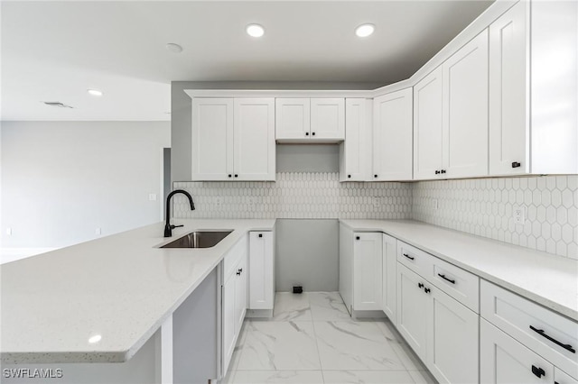 kitchen with white cabinetry, sink, backsplash, and light stone counters