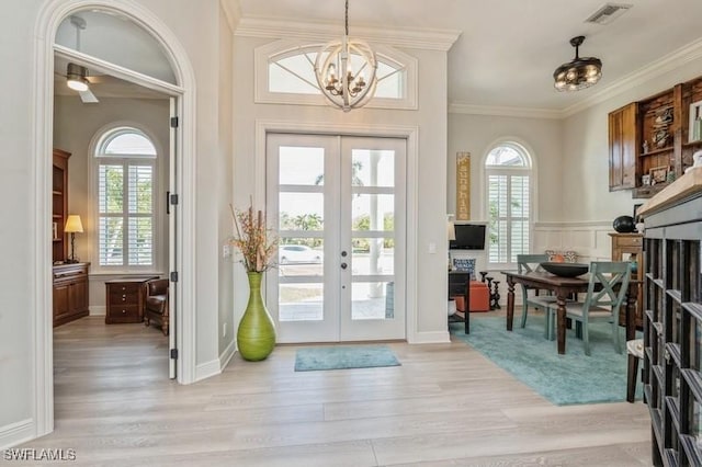 entryway featuring french doors, crown molding, a chandelier, and light wood-type flooring