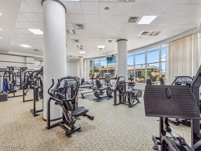 exercise room with carpet floors, decorative columns, and a drop ceiling